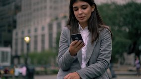 Pretty spanish female in trendy jacket typing text message on smartphone chatting in social networks via 4G connection outdoors on urban settings
