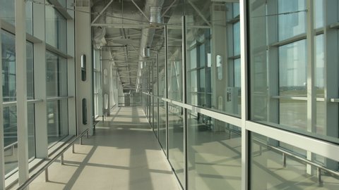 Stylish glass corridor in airport terminal to runway with planes. Transparent panoramic windows with amazing view on airfield. Empty path, escalator on right.