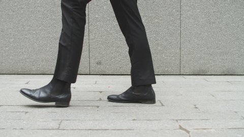 A man in black business trousers and shoes is walking around the city and dancing.