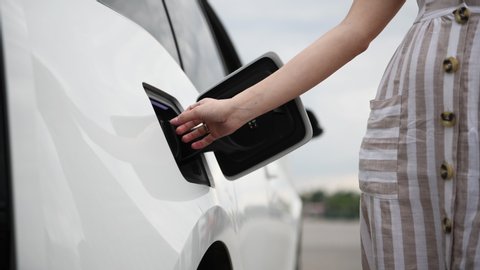 Woman plugs in charger into socket of her modern new electric car.