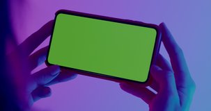 GREEN SCREEN CHROMA KEY CU Caucasian female holding generic smart phone, horizontal orientation, colorful neon background. 4K UHD RAW Graded footage