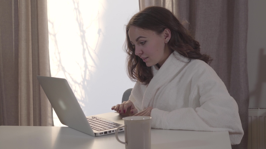Portrait of young pretty Caucasian girl surfing Internet at home. Beautiful brunette woman using laptop and making faces as looking at screen. Internet, online, social media. | Shutterstock HD Video #1042772101