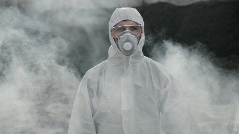 Portrait of a laboratory assistant in a mask coming out of poisonous smoke with a tool box