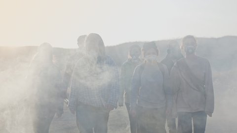 Group of young people in gas mask going through the toxic smoke in a desolate and burned out forest landscape.