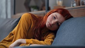 upset teenage girl lying on sofa and looking at camera