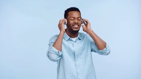 african american man in headphones dancing isolated on blue