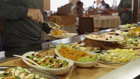 Buffet table at all you can eat restaurant. woman hand take fresh food salad in cafeteria. Self service meals. Catering, public cafe lunch. sliced meat on plates at breakfast smorgasbord table