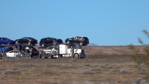 CLOSE UP Freight truck hauls cars down a highway crossing the Utah desert. Cargo lorry speeds along the interstate freeway while transporting brand new cars across the country. Hauling cars across USA