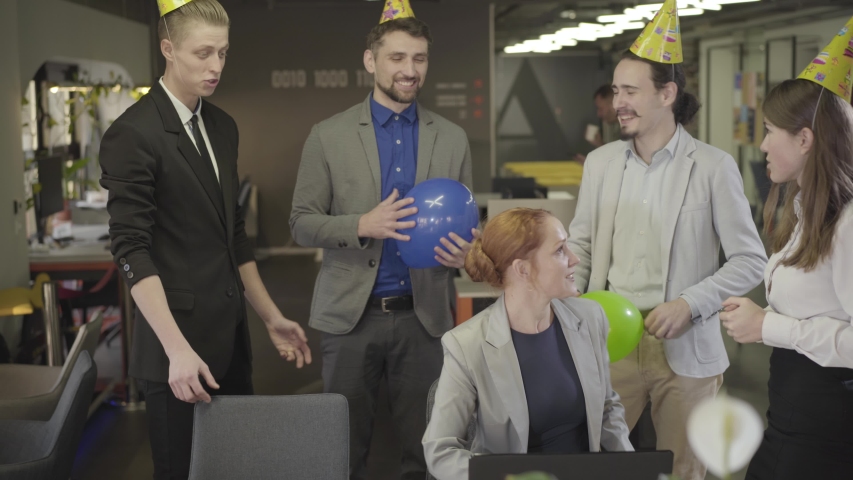 Joyful Caucasian office workers congradulating their colleague with birthday. Positive coworkers partying in open space office. Event, party, happiness, celebration.