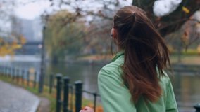 Back view of sporty girl in earphones running in autumn city park on riverside