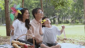Scene of happy Asian family, grandmother, mother and son picnic at the park in the afternoon, blowing bubble while mom holding colorful windmill, family spending happy time together, outdoor activity. - Powered by Shutterstock - Get 15% off with code: PIKWIZARD15