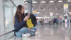 4K handheld clip with young pretty girl sitting on the floor of airport, she use smartphone calling to someone during waiting for journey together