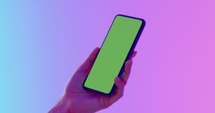 GREEN SCREEN CHROMA KEY CU Caucasian female using generic smart phone, vertical orientation, colorful neon background. 4K UHD RAW Graded footage