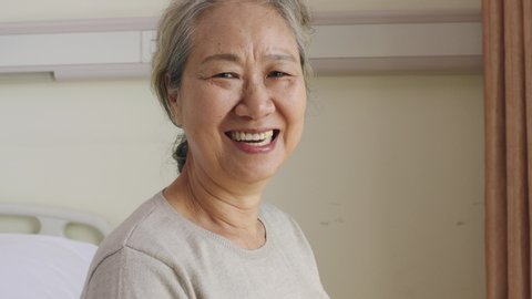 senior asian woman sitting in wheel chair by the window turning to camera smiling