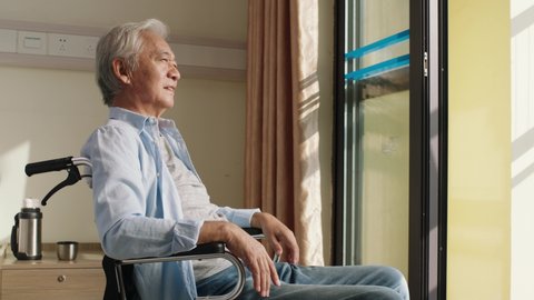 asian old man sitting in wheel chair in his room in nursing home looking happy and content