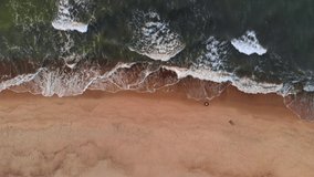 Aerial view A video of a tropical beach at sunset showing evening aerial footage of green foaming ocean waves crashing onto the coastline. Top view without people