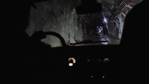 The car drives in a dark gloomy mine tunnel, illuminated by lanterns. View from inside the car, descends underground, into the mine.
