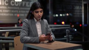 Concentrated spanish female millennial sending text messages via smartphone using 4G connection for checking male in cafe after work
