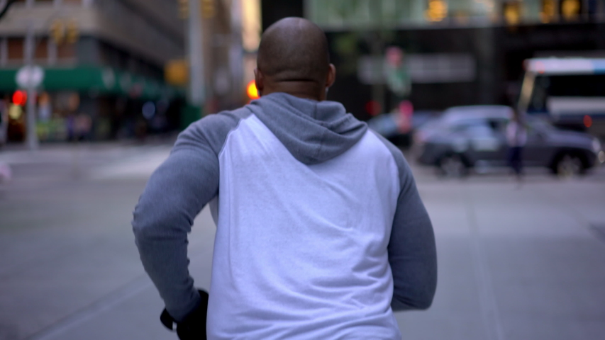 Back view of dark skinned male jogger listening music running on one place waiting for crossing road in avenue downtown 
