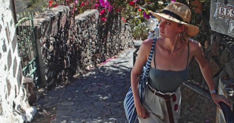 Tenerife, Spain - August 12, 2019: Attractive young woman in fashion summer look walking in spanish village on summer day. Pretty girl in sun hat walks up exploring tourist route in Masca, Tenerife.