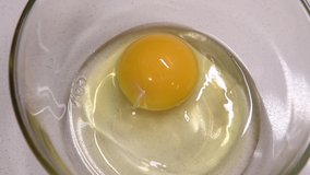Video top view of a woman using a fork to mix up a raw egg to use as scrambled eggs, omelet or egg wash on pastry. Real time 4K video stirring one organic free range egg in clear glass bowl.