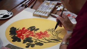 Guy drawing flower with watercolor on the paper with yellow background nearly finish on the table, nearby have many color and palette