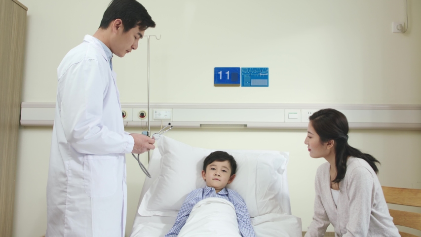 young asian male doctor making rounds examining and talking to child patient and mother in hospital ward Royalty-Free Stock Footage #1042879063