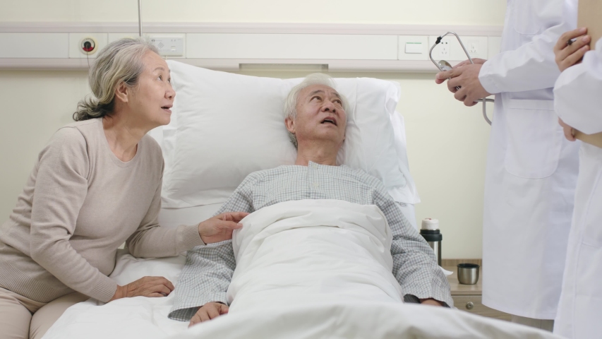 Two young asian doctors making rounds talking to senior patient in hospital ward | Shutterstock HD Video #1042879069