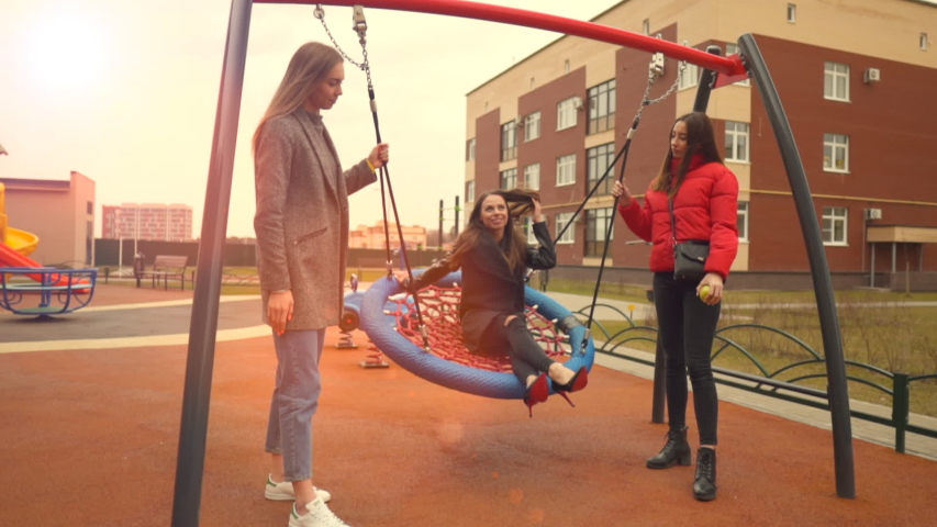 Young group of female friends spending time in the park on swing