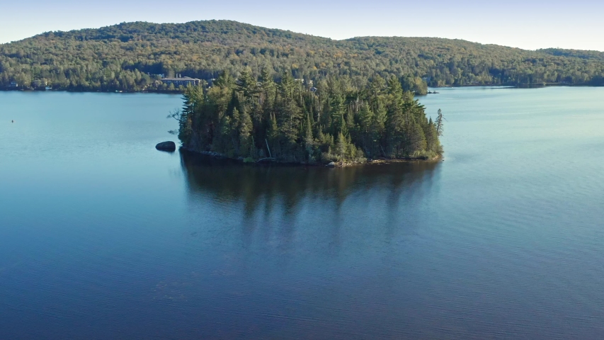 Aerial flying over people canoeing on calm lake with island in the middle. Lac Superieur, Mont Tremblant, Quebec, Canada. 