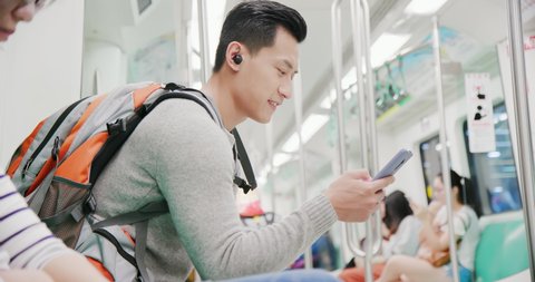 asian man use wireless earbuds to listen music or watch video on the train