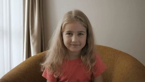 Kid Child Girl Making Online Video Call Recording Vlog Sitting On Sofa , Portrait. Funny Girl Smiling Looking At Camera. Happy Cute Little Vlogger Saying Hello Hi Looking At Camera Talking To Webcam.