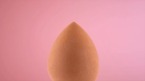 Makeup liquid foundation pouring on make-up blender sponge, closeup. Foundation beauty facial cosmetics, tool for perfect make up. Dripping bb cream or concealer. over pink background. 4K slow motion