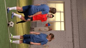 Vertical format video of young female athletes in uniform playing soccer on indoor sports field while their friends and relatives cheering for them with pompoms and poster