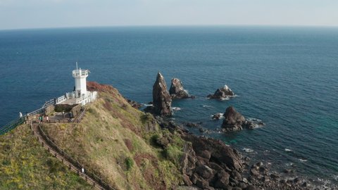 Drone view flying towards the sea. Take a drone of the white lighthouses of the coastal cliffs, the vast ocean, the big waves and the rocks. Aerial View. Jeju Island.