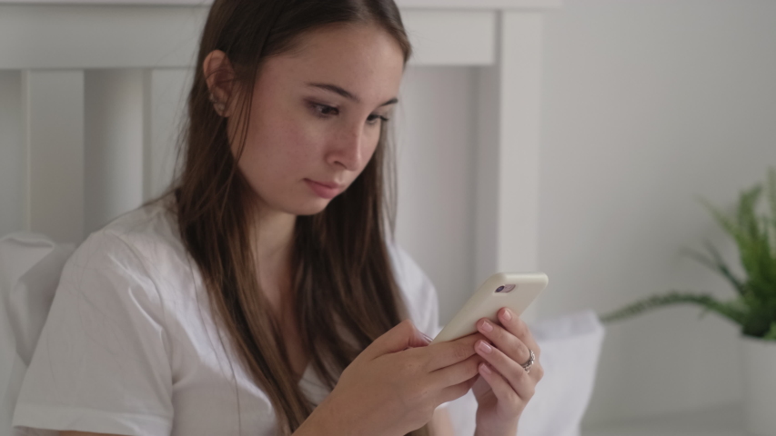 Dark-haired girl starts her morning with checking social media messages and posts on smartphone | Shutterstock HD Video #1042919386