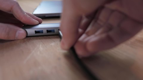 Plugging in usb cable into usb-c hub connected to a laptop on wooden desk
