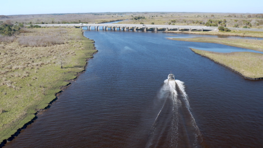 Drone Aerial - AIRBOAT passing under a highway bridge during wildlife tour through Florida wetlands on the blue water St Johns river near Orlando and Titusville.