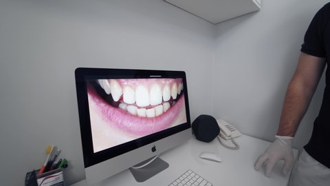 VINNITSA, UKRAINE - August 2019: Young woman looking at her teeth on a screen. Dentist showing to a female patient photo of her smile on the monitor on the modern medical room background.