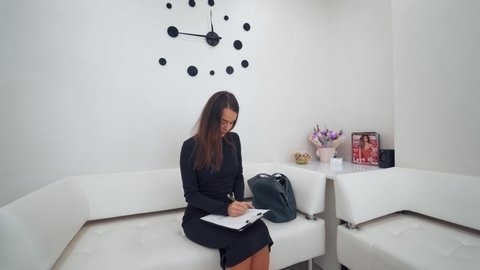 VINNITSA, UKRAINE - August 2019: Young woman in the waiting room. Beautiful girl filling the form in the reception of the clinic. Interior of the modern center.