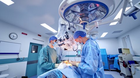 Operation through the microscope. Two surgeons use medical instruments while perform an operation. Specialists looking into the microscope in the modern operating room.