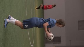 Vertical format video of professional female soccer player heading ball while practicing with teammates on indoor sports field