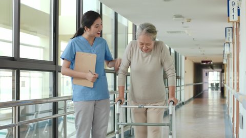 young asian physical therapist working with senior woman on walking using a walker in rehab center or nursing home