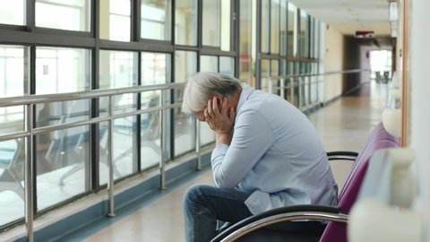 sad and depressed asian old man sitting in chair in hospital corridor 