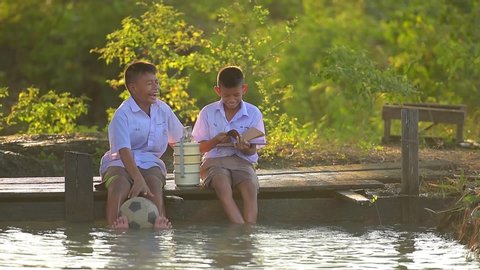  Asian student reading book with school uniform with football and Food carrier on the wood bridge in the rice fields  countryside Thailand country. Rural concept.