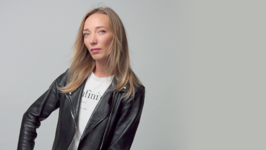 free hand camera movement. Blonde caucasian blue eyed model alone in studio. Wears a leather jacket, blowing hair