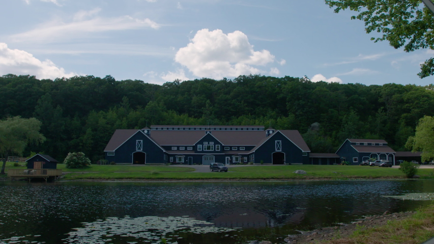 Timelapse of shifting light over Majestic Blue Horse Stables on green farmland