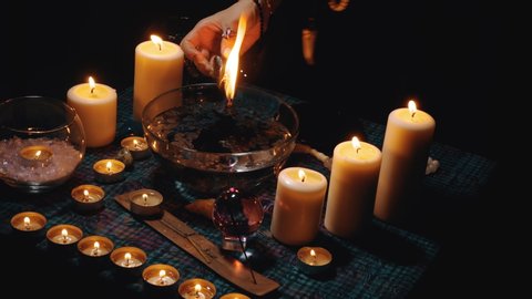 Fortune teller hold a black burning candle above a bowl of water. Hot wax dripping into water. Rite of black magic and occultism. Occult, esoteric and divination concept.