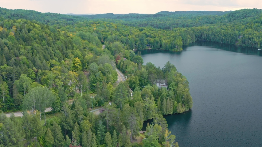 Aerial flying over a tranquil forest and calm blue lake. Quebec, Canada 