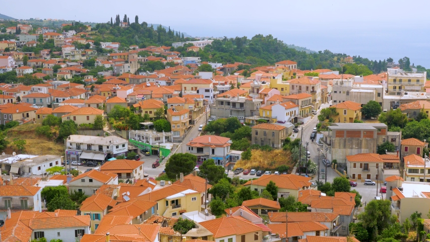 Cityscape with red roofs and mountains on background. Traveling concept. Mountain town, view from the top. Greek city scape with white houses, red roofs and green trees among houses. Traveling concept | Shutterstock HD Video #1042968322